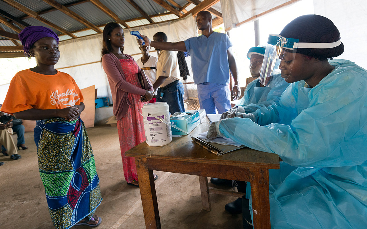 Vor einem Krankenhaus in Liberia kontrolliert ein Mitarbeiter mit einem Infrarot-Thermometern die Temperatur der ambulanten Patienten. Photo: Christoph Püschner/Diakonie Katastrophenhilfe